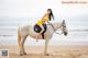 A woman in a yellow bikini riding a white horse on the beach.