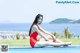 A woman in a red bathing suit sitting on the edge of a swimming pool.