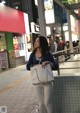 A woman standing on a sidewalk holding a white bag.