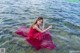 A woman in a red dress sitting in the water.