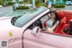 A woman sitting in the driver's seat of a pink sports car.