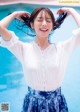 A woman in a white blouse and blue skirt standing by a pool.