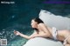 A woman in a white bikini laying on a white pillow by a pool.