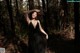 A woman in a black dress standing in the woods.