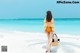 A woman walking on the beach carrying a bag.