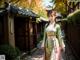 A woman in a green and pink kimono standing in front of a building.